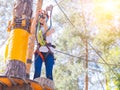 Kid in orange helmet climbing in trees on forest adventure park. Girl walk on rope cables and high suspension bridge in