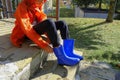 Kid in orange raincoat putting on blue rubby boots sitting on stairs in backyard. Clothing for rainy weather