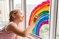 Kid painting rainbow during Covid-19 quarantine at home. Girl near window. Stay at home Social media campaign for coronavirus