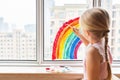 Kid painting rainbow during Covid-19 quarantine at home. Girl near window. Stay at home Social media campaign for coronavirus Royalty Free Stock Photo