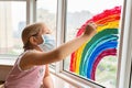 Kid painting rainbow during Covid-19 quarantine at home. Girl near window. Stay at home Social media campaign for coronavirus Royalty Free Stock Photo