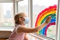 Kid painting rainbow during Covid-19 quarantine at home. Girl near window. Stay at home Social media campaign for coronavirus Royalty Free Stock Photo