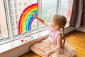 Kid painting rainbow during Covid-19 quarantine at home. Girl near window. Stay at home Social media campaign for coronavirus Royalty Free Stock Photo