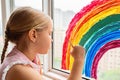Kid painting rainbow during Covid-19 quarantine at home. Girl near window. Stay at home Social media campaign for coronavirus Royalty Free Stock Photo