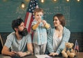 Kid with parents in classroom with usa flag, chalkboard on background. American family sit at desk with son. Patriotic