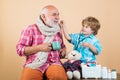 Kid play doctor with dad on color background. Charming little boy examining a cheek of his grandfather. Healthy and