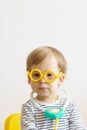 A kid play doctor in the nursery. A boy in yellow glasses sits on the chaur with a medical suitcase filled with Royalty Free Stock Photo