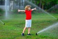 Kid play in garden near irrigation watering sprinkler system. Watering grass with automatic sprinkler. Lawn and Royalty Free Stock Photo