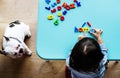 Kid playing with alphabetic toys sitting next to pet dog