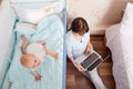 Kid playing in bed, mum pajamas works with the laptop I got close to the child in the room. A busy mom. Royalty Free Stock Photo