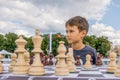 Kid playing chess at chessboard outdoors. Boy thinking hard on chess combinations