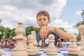 Kid playing chess at chessboard outdoors. Boy thinking chess combinations