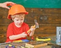 Kid playing with hammer. Daddy holding hardhat on sons head. Concentrated kid in workshop