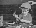 Kid playing with hammer. Daddy holding hardhat on sons head. Concentrated kid in workshop