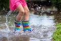Kid playing out in the rain. Children with umbrella and rain boots play outdoors in heavy rain. Little girl jumping in muddy Royalty Free Stock Photo