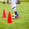 Kid playing soccer. Training football session for children. Boys is training with soccer ball and bollards on the field