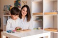 Kid playing with a tetris wood puzzle and mother or teacher help. Homeshooling. Learning Community. Montessori School