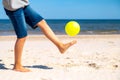 Kid playing with yellow beach ball on the sand by the sea water on a sunny day. Copy space for text. Vacation background Royalty Free Stock Photo