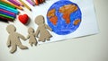 Kid putting paper family and heart sign near Earth painting, saving planet