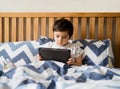 Kid reading bed time stories on tablet before sleep, Happy boy sitting in bed playing games on digital pad, Child relaxing at home Royalty Free Stock Photo