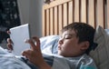 Kid reading bed time stories on tablet before sleep, Happy boy sitting in bed playing games on digital pad, Child relaxing at home Royalty Free Stock Photo