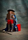 Kid reading book. Little girl wearing costume of prince, musketeer and royal person sitting and reading over dark