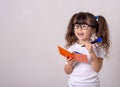 Surprised cute child in eyeglasses, writing in notebook using pencil, keeping mouth wide open. Four or five years, isolated