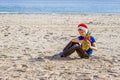 Kid in red Santa hats and pineapple as Christmas tree sitting at sea beach during Christmas vacation