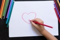 Kid`s hand with pencil draws heart on white paper. Mother`s day concept. Celebration. Hand made card.