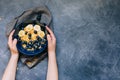 Kid`s hands hold Dark blue bowl of oatmeal porridge with banana and blueberry on vintage table top view in flat lay