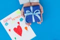 Kid`s hands holding gift box with child`s drawing on blue background. Concept Father`s Royalty Free Stock Photo