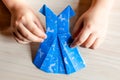 Kid`s hands holding origami made blue dress from butterfly printed paper. Mother`s day, birhday, summer gift concept. Family