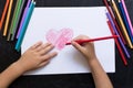 Kid`s hands with pencil draws heart on white paper. Mother`s day concept. Celebration. Hand made card. Top view.