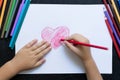 Kid`s hands with pencil draws heart on white paper. Mother`s day concept. Celebration. Hand made card. Top view.