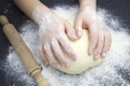 Kid`s hands, some flour, wheat dough and rolling pin on the black table. Children hands making the rye dough for backing bread. Royalty Free Stock Photo