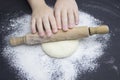 Kid`s hands, some flour, wheat dough and rolling pin on the black table. Children hands making the rye dough for backing bread. Royalty Free Stock Photo