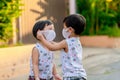 Kid in safety wearing mask in town. Twin Children wearing medical face mask outdoor. Twin Child helps to put a mask on his face t