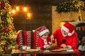 Kid Santa Claus enjoying in served gingerbread cake and milk. Santa Father and son having fun near Christmas tree and Royalty Free Stock Photo