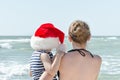 Kid in Santa hat in the arms of mother, the beach. Back view