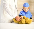 Kid with serious face plays doctor. Little assistant examines bear