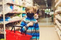 Kid with shopping basket in supermarket. Child wears protected mask in shop