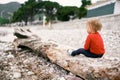 Kid sits on a pebble beach on an old deck. Back view Royalty Free Stock Photo