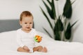 The kid sits in a snow-white bed, laughs and plays with a rattle. Royalty Free Stock Photo