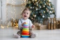 The kid, sitting on the floor near a smart Christmas tree, collects a multicolored pyramid. Royalty Free Stock Photo