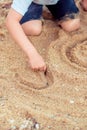 Kid is sitting on the sand on the baech ang drawing on the sand Royalty Free Stock Photo