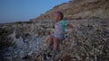 Kid sitting on the stones on the sea coast at sunset . Boy talking and fidgeting