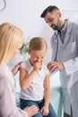 Kid sneezing near mother and doctor