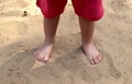 Kid standing bare footed on the sand in red shorts. Child`s feet with cute toes, happy feeling, warm sumer day, Earth day Royalty Free Stock Photo