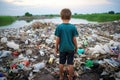 Kid standing near landfill next to mountain of plastic wastes looking far into hopelessness Royalty Free Stock Photo