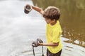 A kid stands in the river on outdoor and destroys a mirrorless photo camera. The concept of obsolescence of technology.